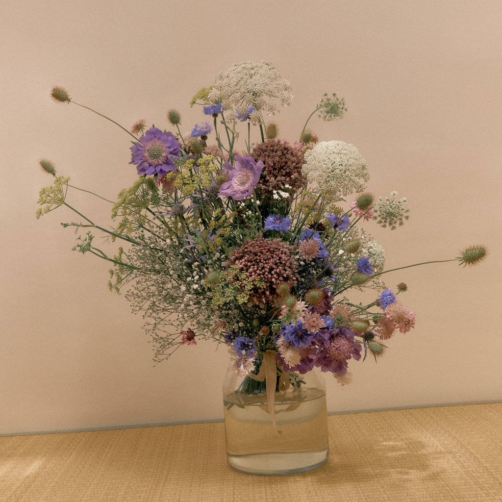 Bouquet of wildflowers in a clear vase on a beige surface with a beige background