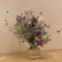 Bouquet of wildflowers in a clear vase on a beige surface with a beige background