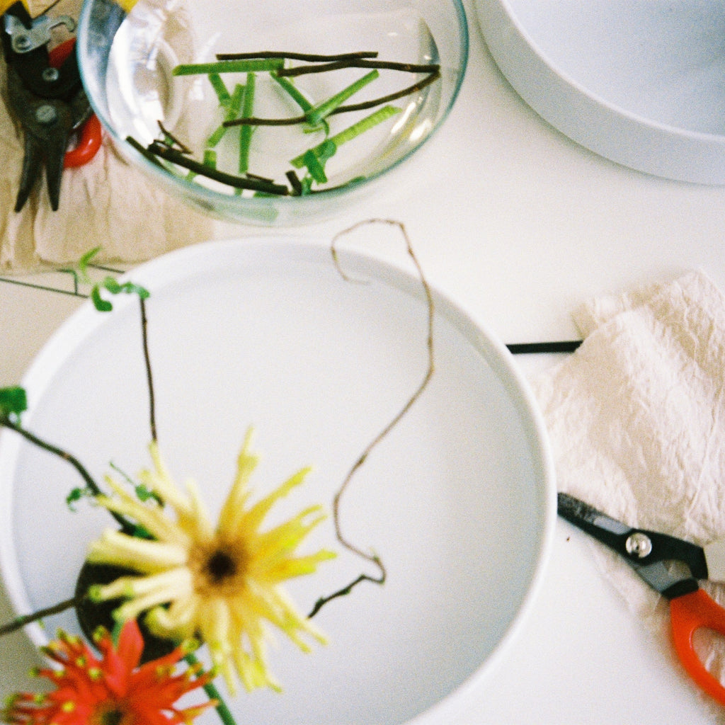 Floral arrangement setup with scissors and water on a white surface